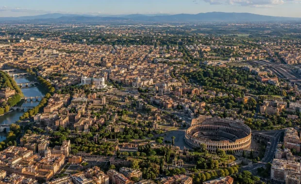 Aerial view of Rome showing the historic center, dense neighborhoods, rail lines, green space, and outer development
