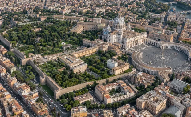 High aerial view of Vatican City showing Saint Peter Square, basilica, gardens, walls, and surrounding Rome